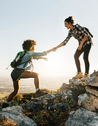 Two women hiking; one reaches down to help the other up a rock