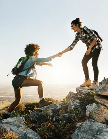 Two women hiking; one reaches down to help the other up a rock